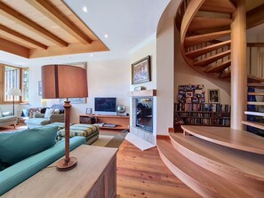 A spacious living room with a curved staircase, a fireplace, and a bookshelf. - Nice apartment for 12 people with WIFI, TV, terrace, pets allowed and panoramic view (Crans-montana)