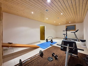 Ein Heimfitnessraum mit Klimmzugstange, Gewichtbank, Trainingsmatte, Kettlebells, einem Ergometer und einem Laufband.