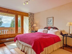 Ein Schlafzimmer mit einem großen Bett, Holzboden, einem Fenster mit Vorhängen und einem gerahmten Bild an der Wand.