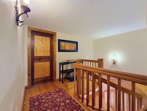 Uma escada de madeira com corrimão, uma porta de madeira, uma pequena mesa com uma tigela e um quadro na parede.