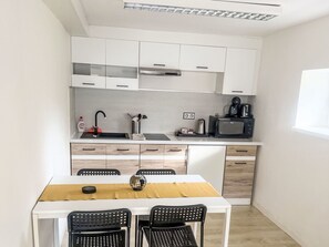 Eine kleine Küche mit weißen Schränken, einer Mikrowelle, einer Kaffeemaschine und einem Essbereich mit zwei Stühlen und einem Tisch.