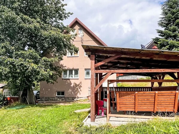 A two-story house with a wooden pergola and a red chair outside.