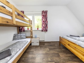 A dormitory room with bunk beds, a window with curtains, a radiator, and a small table.
