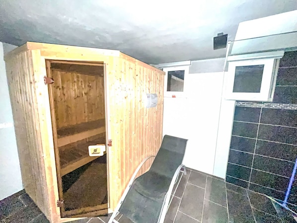 A wooden sauna with a door, a tiled floor, and a wall with a window.