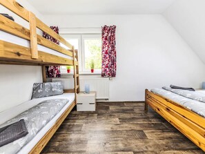Ein Schlafsaalzimmer mit Etagenbetten, einem kleinen Schreibtisch, einer Heizung und einem Fenster mit Vorhängen.