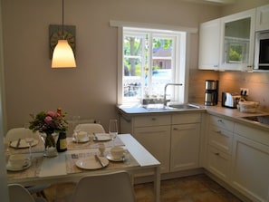 Une cuisine avec une table à manger dressée pour quatre personnes, une fenêtre donnant sur l’extérieur et une machine à café posée sur le plan de travail.