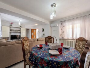 Een moderne woonkamer met een bank, een eettafel en stoelen. Er is een televisie, een open haard en een raam met gordijnen.