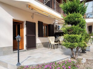 Um edifício residencial com varanda, área de jantar com mobiliário externo e um pequeno jardim florido.