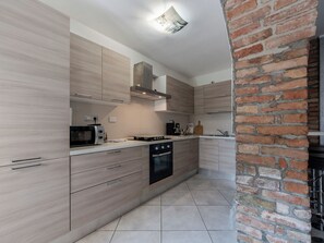 Uma cozinha moderna com armários de madeira clara, forno embutido e parede decorada com tijolos.
