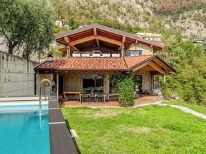 A two-story house with a swimming pool, outdoor seating, and a view of a mountainous landscape.
