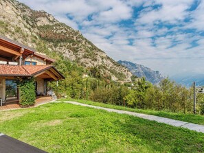 Ein modernes Haus mit Natursteinfassade, einer Holzterrasse und einem Bergpanorama im Hintergrund.