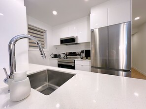 A modern kitchen with stainless steel appliances, a white countertop, and a built-in sink. - Stylish 3BR Condo for Monthly Stays | 2 Baths, Laundry & AC (Montréal)