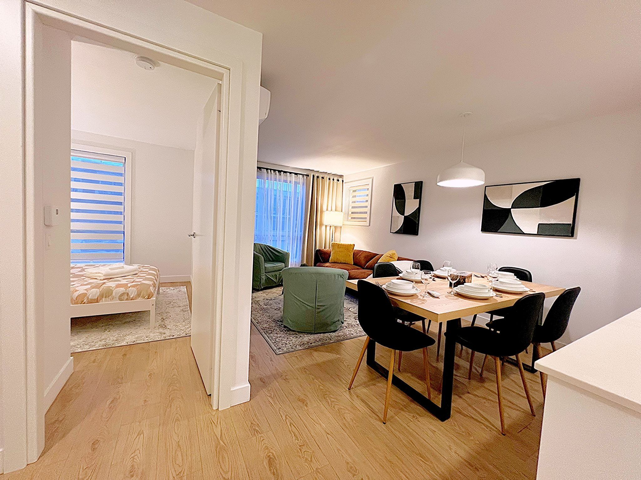 A modern living space with a dining area, a sofa, and a bed with striped bedding.