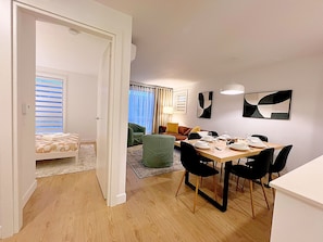 A modern living space with a dining area, a sofa, and a bed with striped bedding. - Stylish 3BR Condo for Monthly Stays | 2 Baths, Laundry & AC (Montréal)