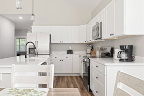 A modern kitchen with white cabinetry, stainless steel appliances, and a wooden dining table. - New 3BR Indianapolis Home  Garage + Laundry (Indianapolis)