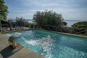 A swimming pool with clear water, surrounded by a wooden deck and lounge chairs, overlooking a body of water and distant mountains. - Villa White Moon with lake view - My Rental Homes (San Feliciano)