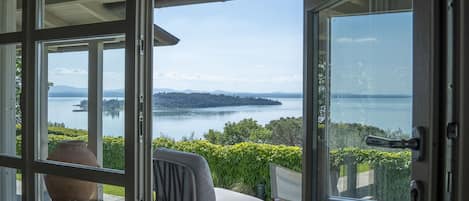 A room with a large glass door leading to a scenic view of a lake and distant land.