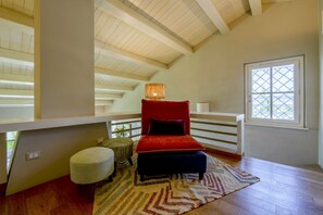 A room with a high ceiling, a red upholstered chair, a small ottoman, a patterned rug, and a window with a lattice design. - Villa White Moon with lake view - My Rental Homes (San Feliciano)