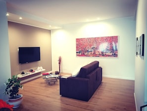 Un soggiorno moderno con una TV a schermo piatto, un divano, un tavolino da caffè e un quadro appeso al muro.