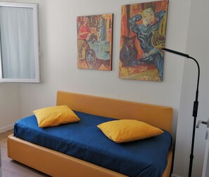 Una stanza con un letto, due cuscini, una lampada da terra e due quadri appesi al muro.