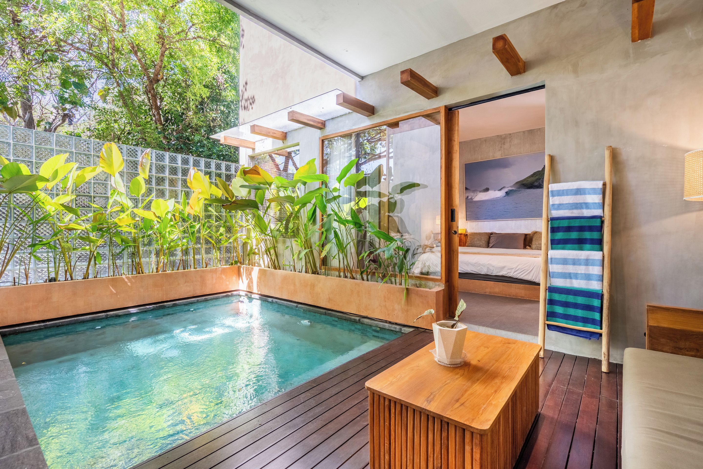 Piscina interior moderna con cubierta de madera, rodeada de abundante vegetación y un gran ventanal.