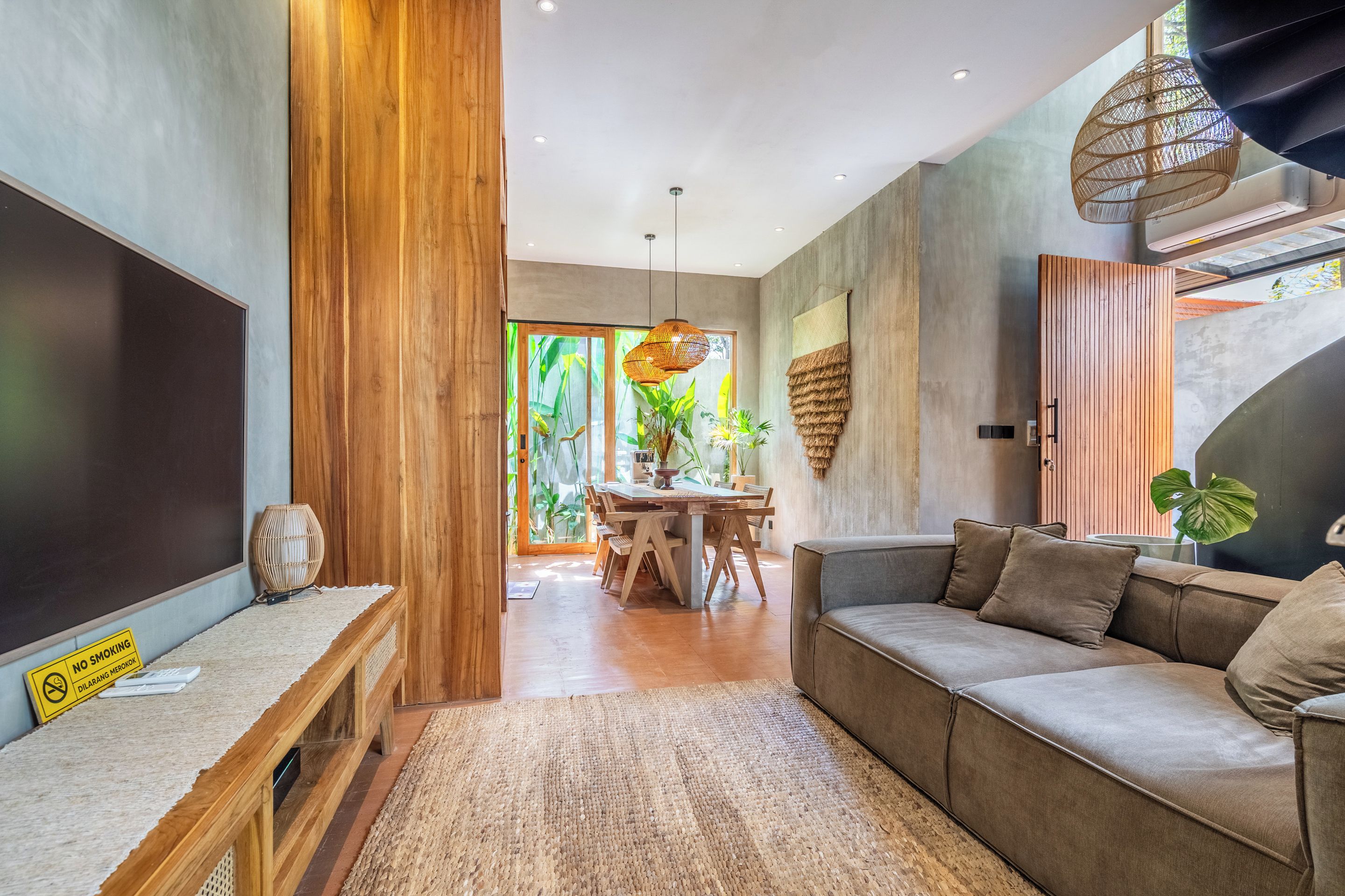Una sala moderna con una pared de acento de madera, un sofá, un área de comedor con una mesa y un amplio ventanal con plantas.