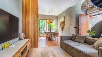 Una sala moderna con una pared de acento de madera, un sofá, un área de comedor con una mesa y un amplio ventanal con plantas.