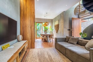 Una sala moderna con una pared de acento de madera, un sofá, un área de comedor con una mesa y un amplio ventanal con plantas.