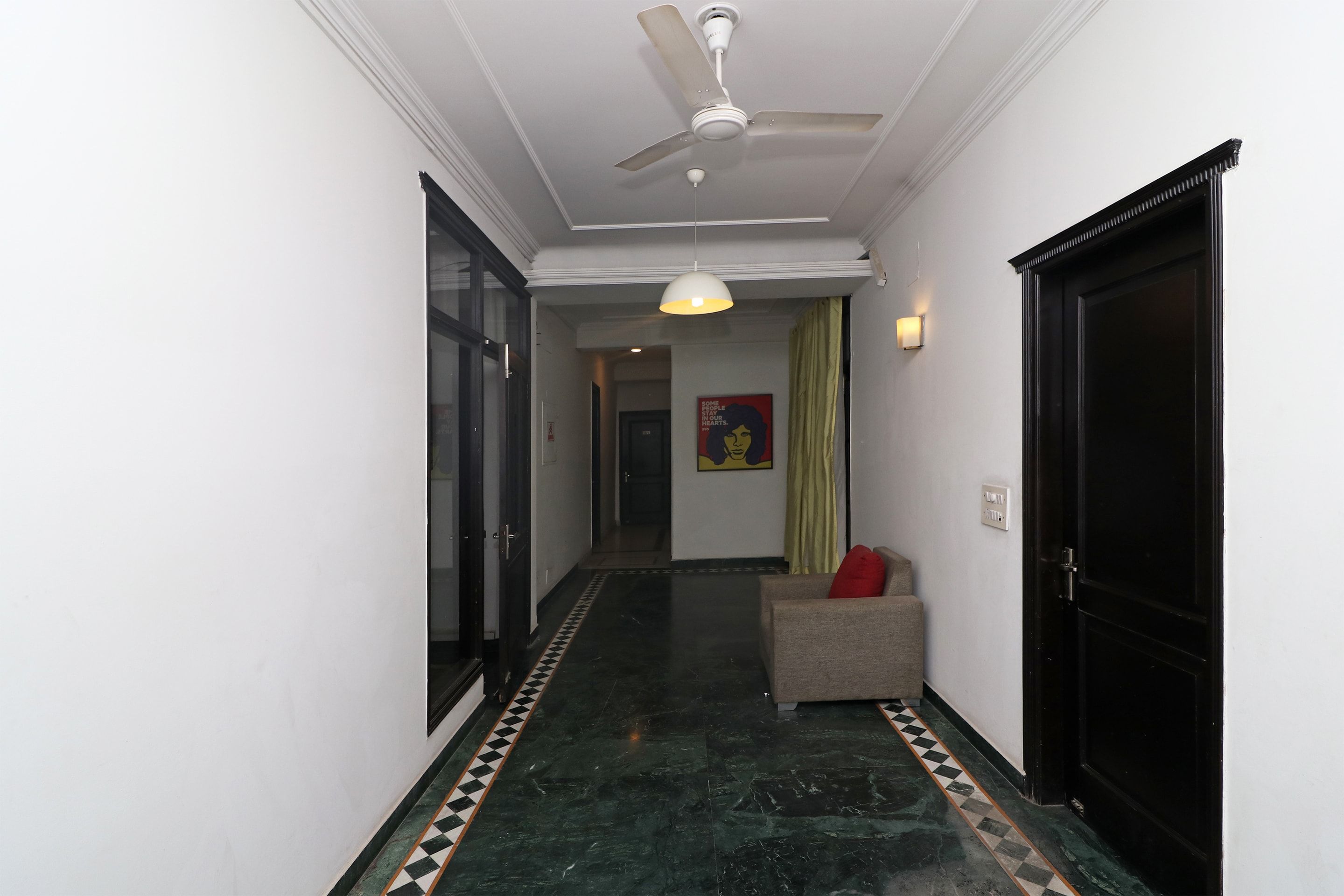 A hallway with a ceiling fan, a sofa with a red cushion, and a patterned floor.