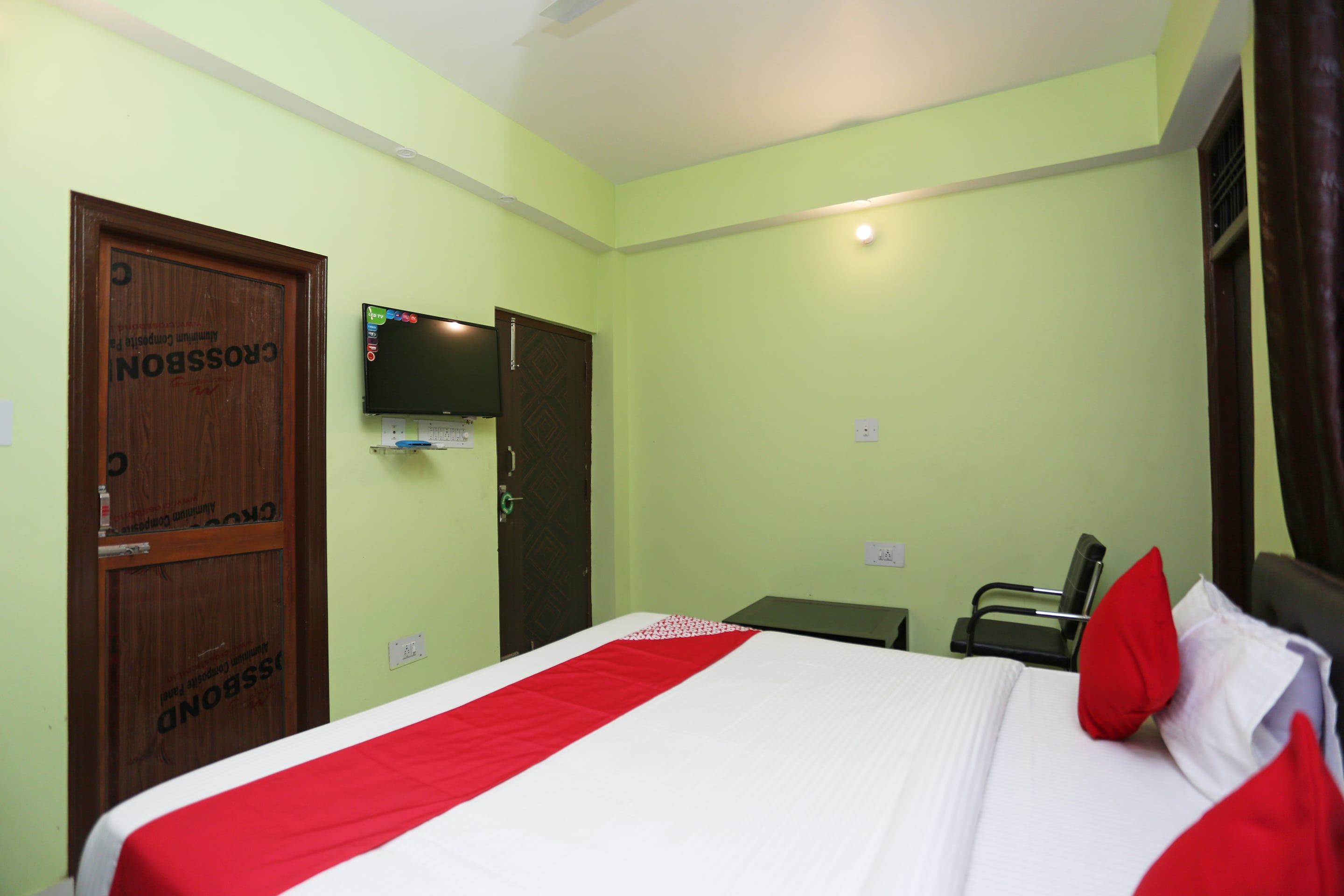 A hotel room with a bed, a desk, a chair, a television, and a door.