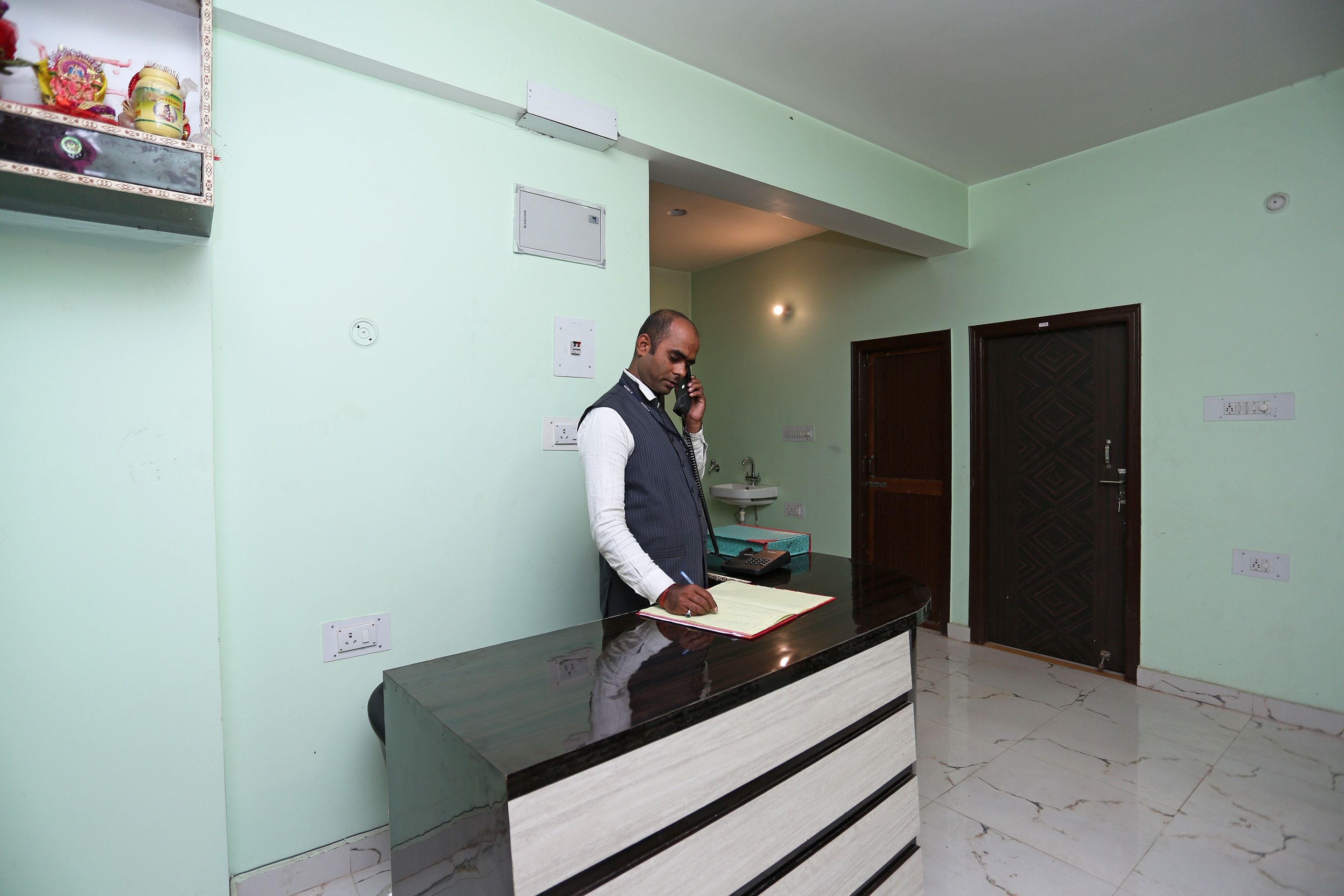 A reception desk with a man standing behind it, a sink, and a door in the background.