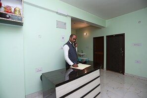 A reception desk with a man standing behind it, a sink, and a door in the background.
