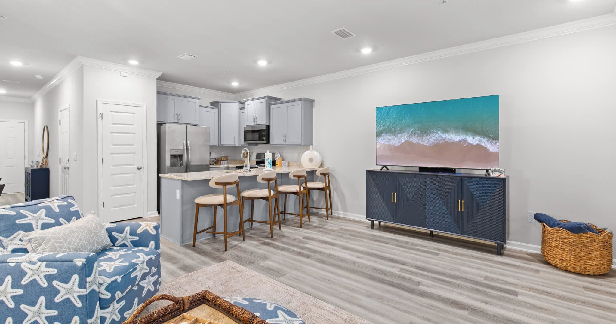 A modern kitchen with a central island, bar stools, and a large flat-screen TV on a cabinet.