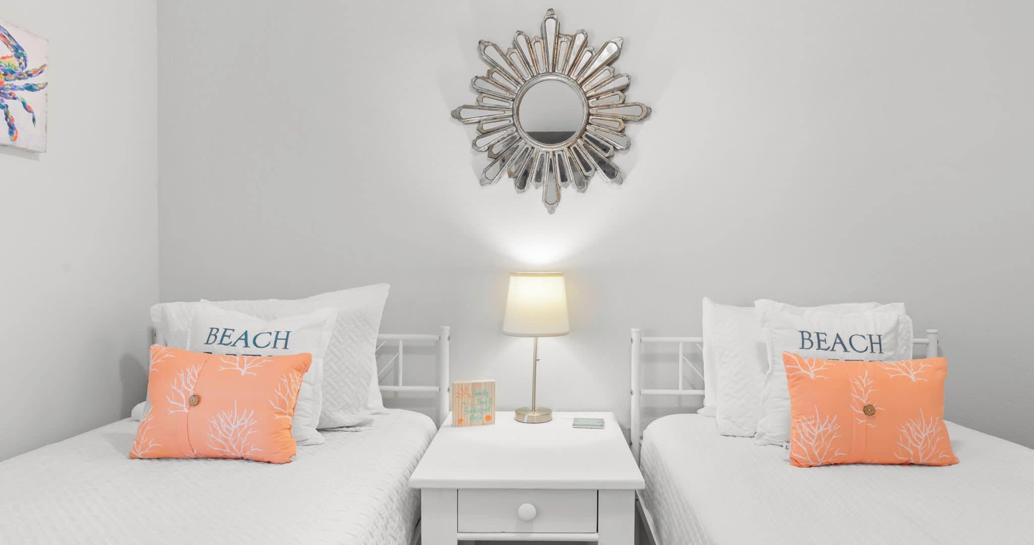 Un dormitorio con dos camas, cada una con una almohada que dice 'BEACH', una mesita de noche con una lámpara y un espejo colgado en la pared.
