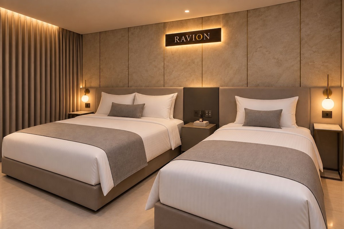 Hotellihuone, jossa on kaksi sänkyä, seinälle kiinnitetty kyltti, jossa lukee ”RAVION”, ja yöpöytävalaisimet.