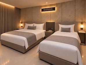 Hotellihuone, jossa on kaksi sänkyä, seinälle kiinnitetty kyltti, jossa lukee ”RAVION”, ja yöpöytävalaisimet.