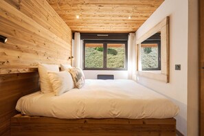 Ein Schlafzimmer mit Holzbalkendecke, einem großen Bett mit weißer Bettwäsche und einem Fenster mit Blick auf Grünflächen.