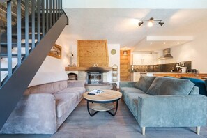 A modern living room with a fireplace, two sofas, a coffee table, and a kitchen in the background. - Geret - Duplex for 6 People | Fireplace | Near the Slopes | Views (Saint-Gervais-les-Bains)