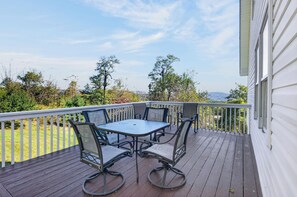A deck with a table and chairs, overlooking a landscape with trees and a distant view. - Four-bedroom Blacksburg home near Virginia Tech with mountain views, front and wraparound porches, fire pit, full kitchen, and basement air hockey. Features 2 king beds, twin room, basement bed, and loft twin beds across 3 levels. (Blacksburg)