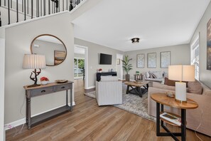 Un salon moderne avec un escalier, un miroir rond, une console, un fauteuil à rayures, un canapé et une table basse.