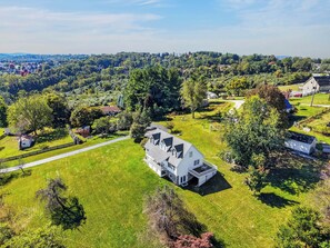 A large white house with a spacious lawn and a driveway. - Four-bedroom Blacksburg home about 1.6 miles from Virginia Tech with mountain views, front and wraparound porches, fire pit, full kitchen, and basement air hockey. Features 2 king beds, twin room, basement bed, and loft twin beds across 3 levels. (Blacksburg)