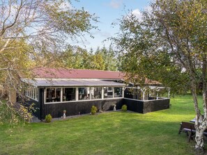 Una casa de dos pisos amb un porxo cobert, envoltada d'un jardí ben cuidat i arbres.