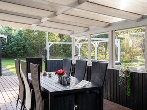 An outdoor patio with a table and chairs, surrounded by a wooden deck and a glass enclosure. - "Ømunde" - 2.5km from the sea by Interhome (Blokhus)