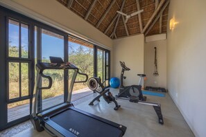Ein Fitnessraum mit Trainingsgeräten, Laufband und Blick ins Freie.