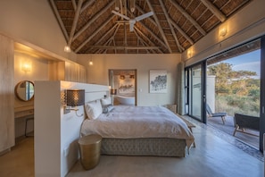 A bedroom with a large bed, a ceiling fan, a bathtub, and a view through a glass door. - Villa Acacia: the most exclusive villa in South Africa (Hoedspruit)