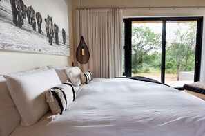 A bedroom with a large bed, a hanging light fixture, and a view of the outdoors through a sliding door. - Villa Umkhaya: Luxury villa with mountain view (Hoedspruit)