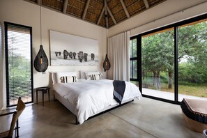 Een ruime slaapkamer met een groot bed, uitzicht op bomen door een raam en een kunstwerk van olifanten aan de muur.