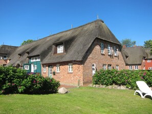 A traditional brick building with a steeply pitched thatched roof, surrounded by well-maintained gardens and a clear sky. - Holiday Apartment With 2 Bedrooms (Wrixum)