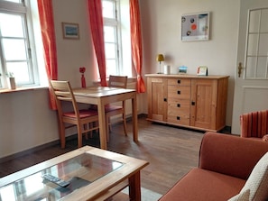 A room with a dining table, chairs, a glass-top coffee table, a sofa, a wooden cabinet, and a door. - Holiday Apartment With 2 Bedrooms (Wrixum)