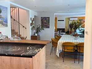 A modern kitchen with a marble countertop, wooden cabinets, and a dining area with yellow chairs and a table. - Une Bastide en Provence (Plan-d'Orgon)